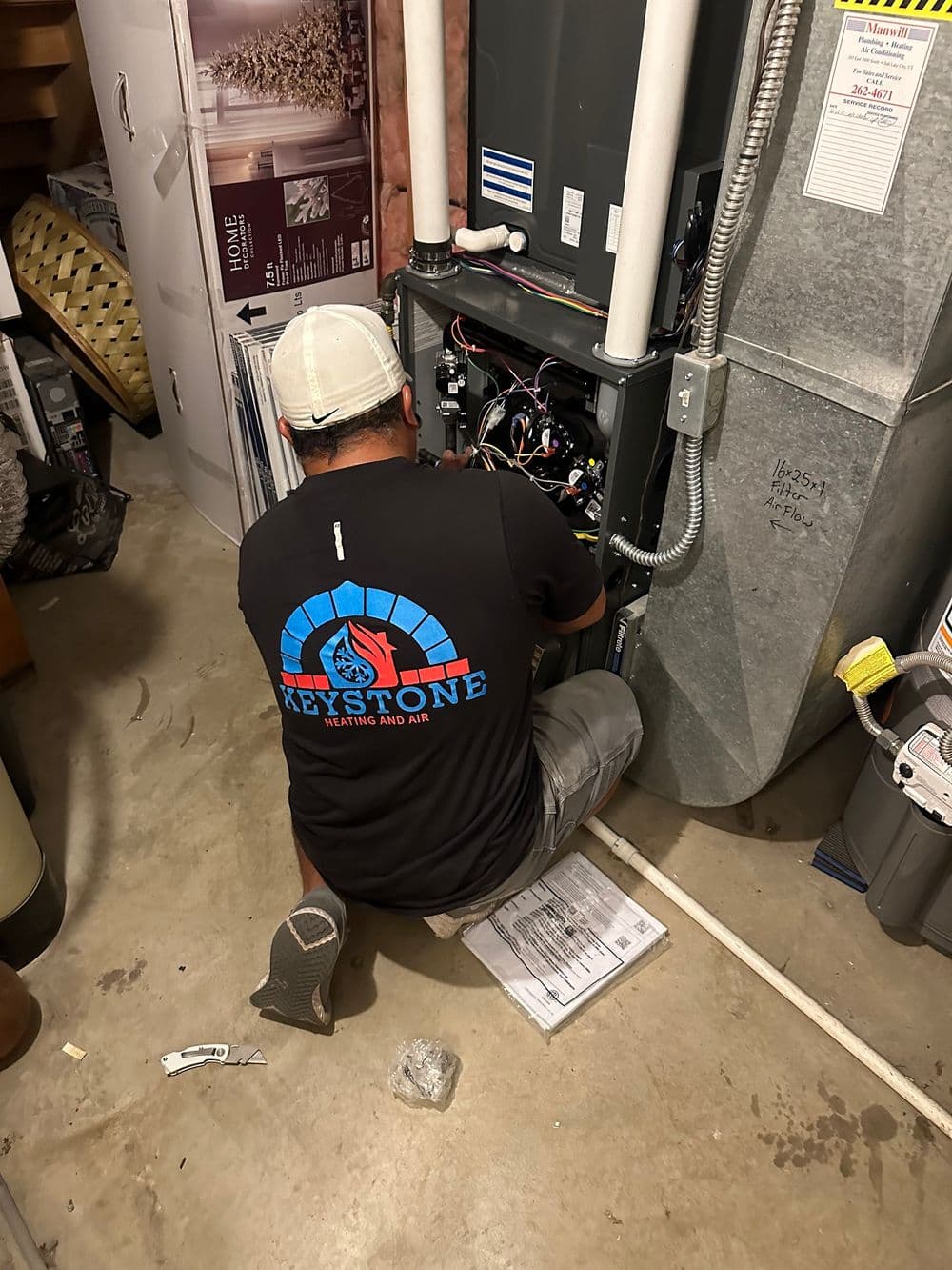 Technician repairing HVAC system in basement with Keystone Heating and Air shirt visible.
