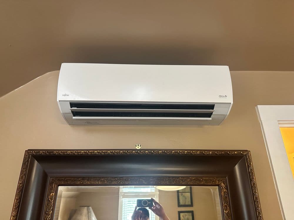 Wall-mounted air conditioning unit above a decorative mirror in a cozy room.