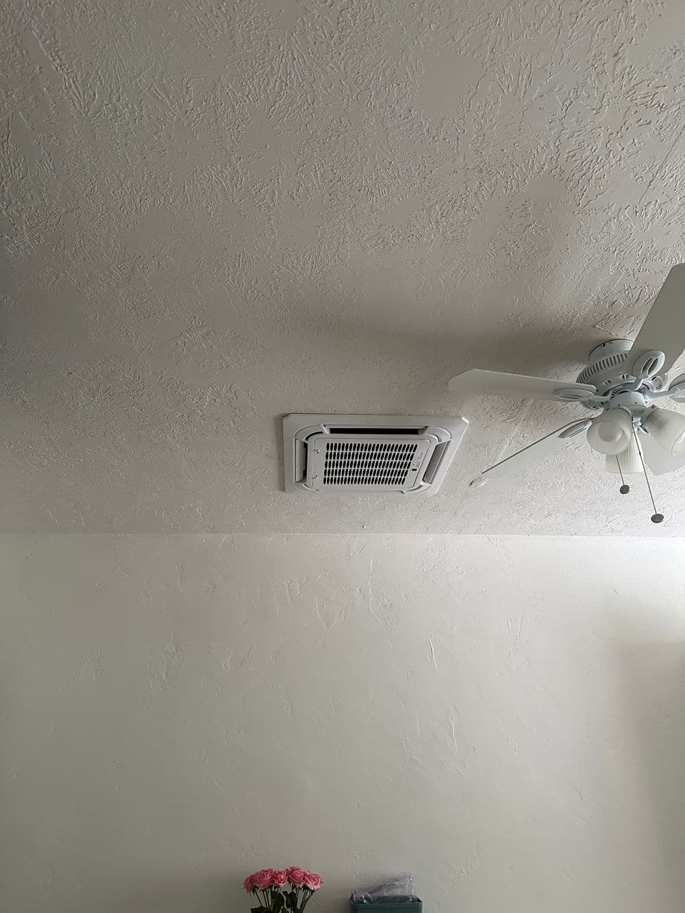 Ceiling-mounted air vent with a fan and floral arrangement in the foreground.