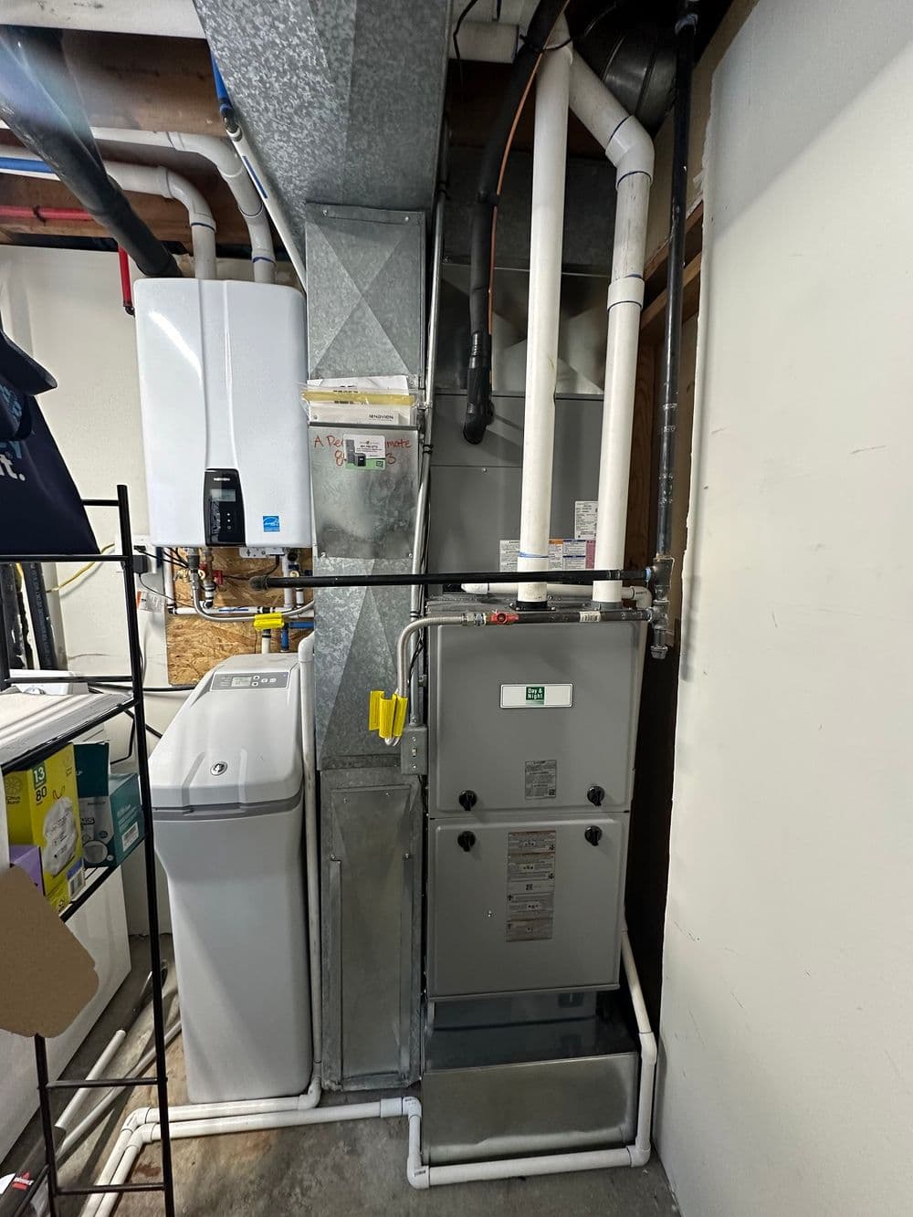 Furnace and water heater in a basement, with pipes and utility shelving in the background.