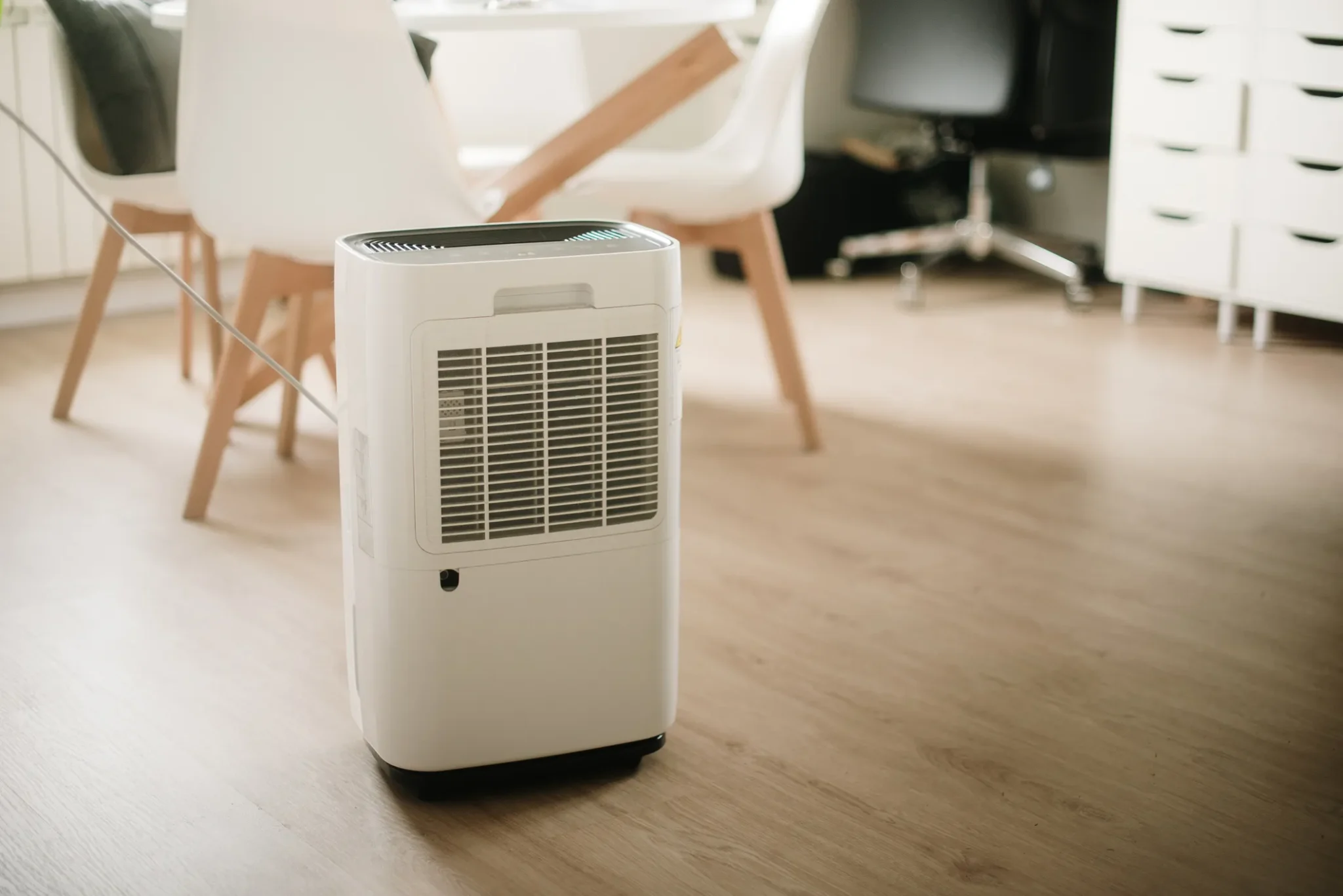 A white dehumidifier is positioned on a wooden floor.