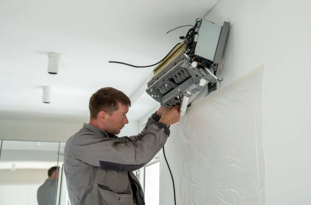 Technician in gray jacket using tools to install or repair wall-mounted air conditioning unit